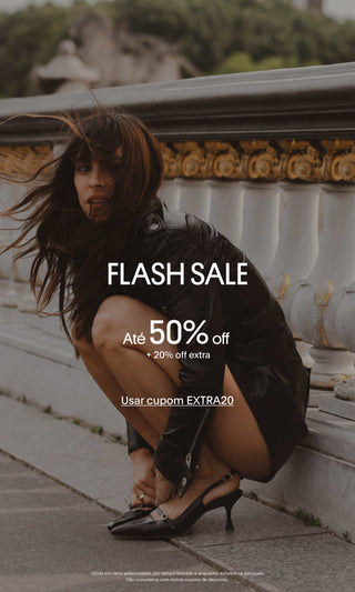 Banner promocional de Flash Sale mostrando uma pessoa agachada em uma calçada ao lado de uma balaustrada de pedra branca, usando jaqueta de couro preta e sapatos slingback pretos de salto baixo. Sobre a imagem, há os textos "FLASH SALE", "Até 50% off", "+20% off extra" e "Usar cupom EXTRA20". Na parte inferior, um aviso informa que a promoção é válida em itens selecionados, por tempo limitado e enquanto durarem os estoques.