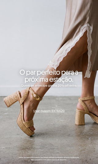 Mulher usando sandálias de salto bloco em ráfia bege com fivela dourada, combinadas com vestido acetinado de renda. Banner promocional com a mensagem "O par perfeito para a próxima estação. Quem se antecipa ganha 20% off extra." e destaque para o cupom EXTRA20.