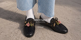 Mocassins de couro preto Cyprus com pompons coloridos, usados com meias brancas e jeans. New In Cyprus — Seu mocassim favorito. Comprar agora.