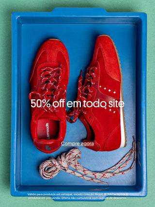Banner promocional com par de tênis vermelhos Larroudé dentro de uma caixa azul, com cadarços extras ao lado. Texto sobreposto: “50% off em todo site” e “Compre agora”. Rodapé informa: válido para produtos em estoque, exceto coleção Nicoló B.; não se aplica a pré-venda; oferta não cumulativa com cupons.
