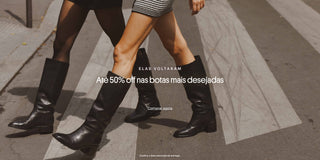 Banner promocional mostrando duas mulheres atravessando uma faixa de pedestres usando botas pretas de cano alto. Texto sobreposto: “Elas voltaram. Até 50% off nas botas mais desejadas”. Botão: “Comprar agora”. Rodapé: “Confira a data estimada de entrega.”