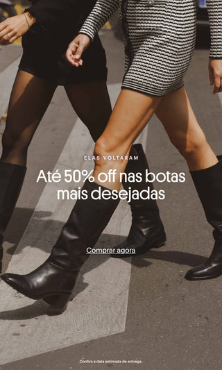 Banner promocional mostrando duas mulheres atravessando uma faixa de pedestres usando botas pretas de cano alto. Texto sobreposto: “Elas voltaram. Até 50% off nas botas mais desejadas”. Botão: “Comprar agora”. Rodapé: “Confira a data estimada de entrega.”