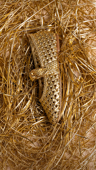 Sapato dourado trançado Larroudé sobre fios metálicos dourados em composição de produto.