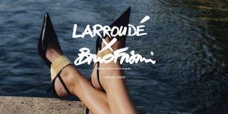 Pernas cruzadas sobre mureta à beira d'água usando scarpin slingback preto de bico fino com tornozeleira dourada – Larroudé x Bruno Frisoni