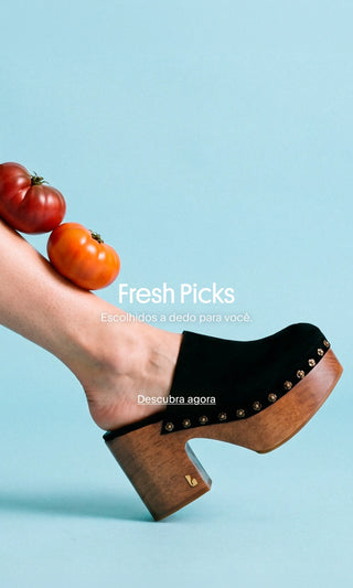 Fresh Picks: tamanco preto com salto de madeira e tomates apoiados sobre a perna.

