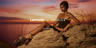 Modelo usando vestido tomara que caia preto e sandálias plataforma Larroudé by Nicolò B. sentada sobre rochas ao pôr do sol, com o mar ao fundo e identidade visual da colaboração ao centro da imagem.